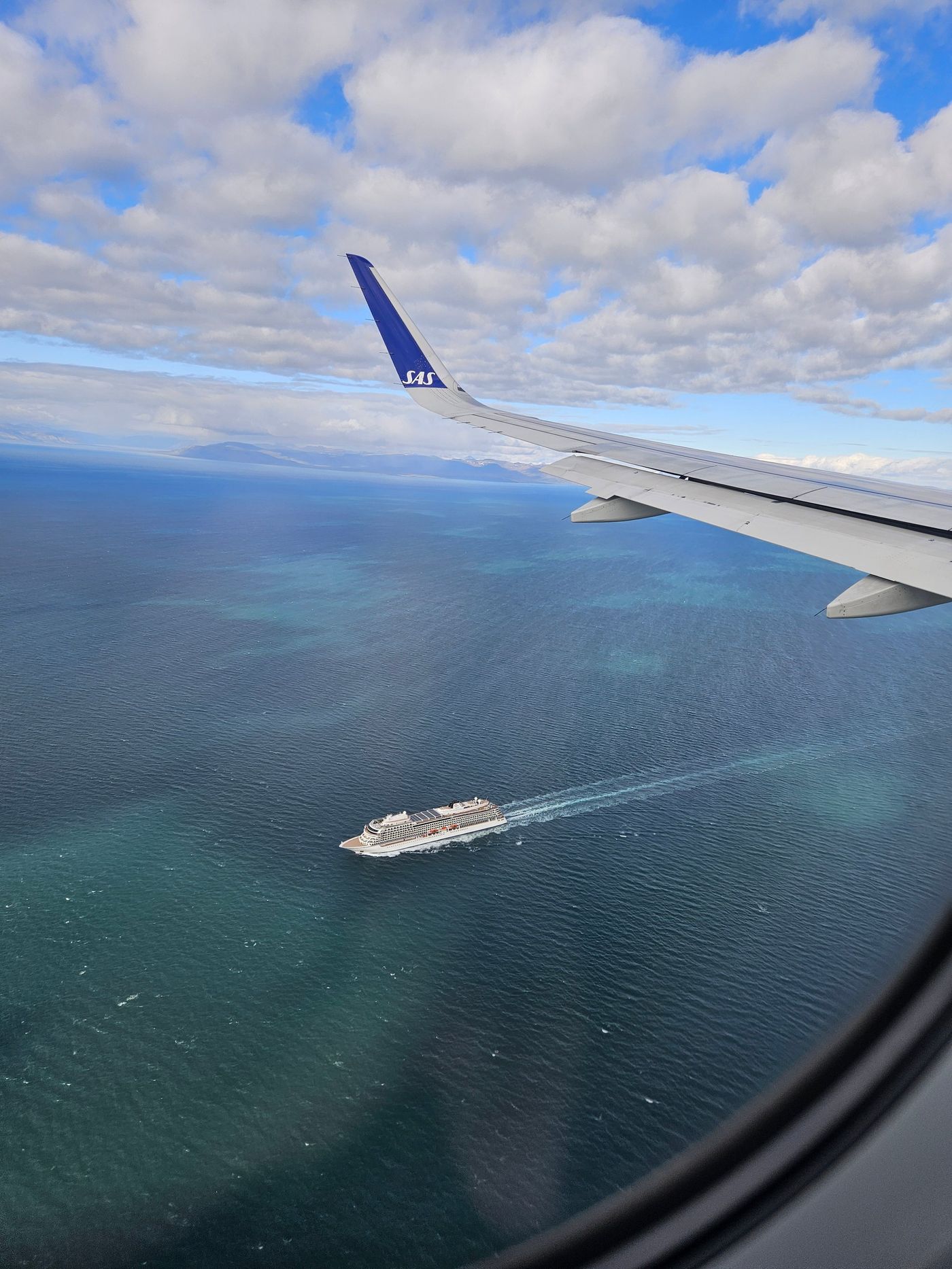 A single ship draws its wake across the fjord below