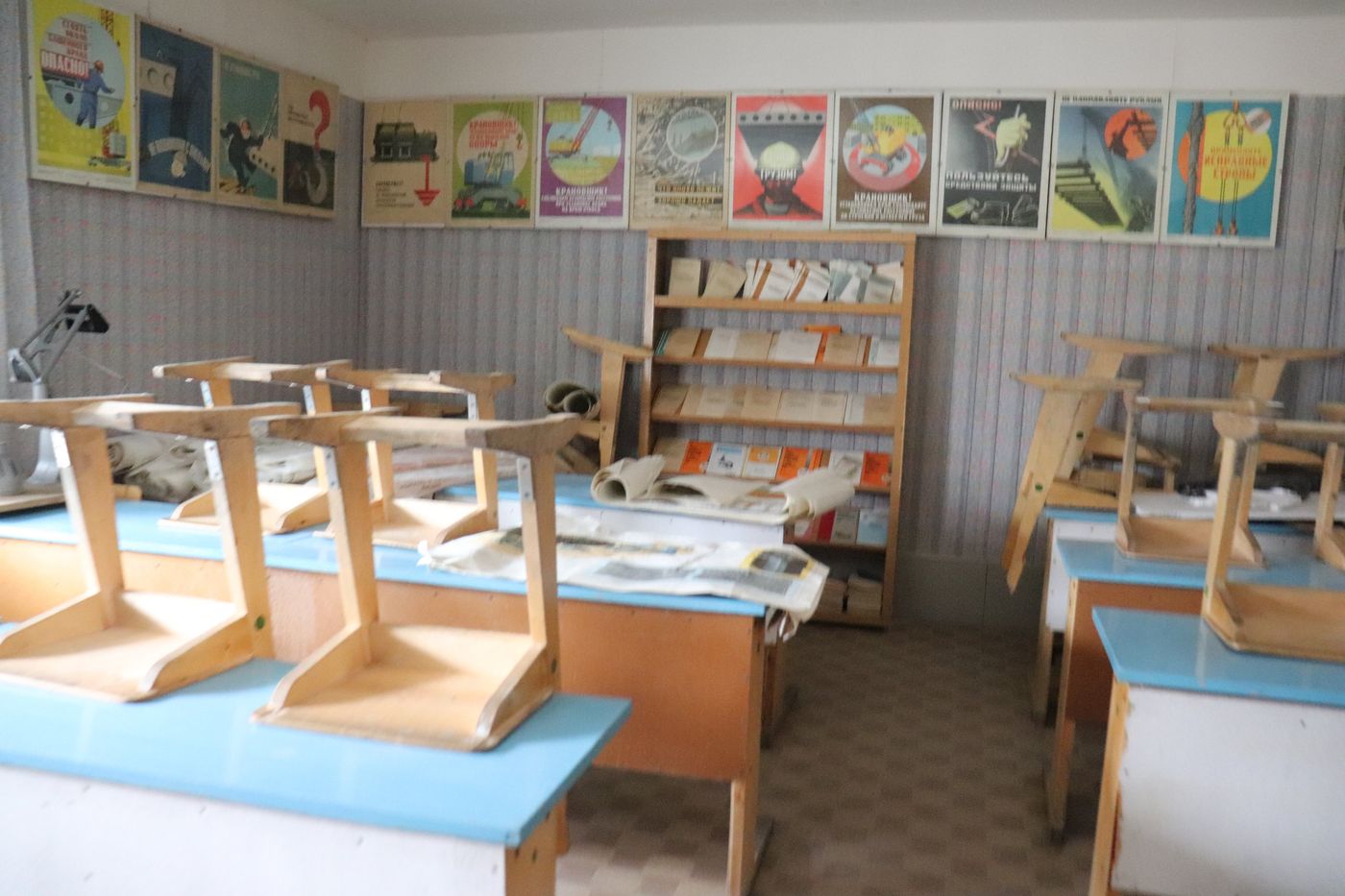 Small chairs stacked in a schoolroom hung with posters