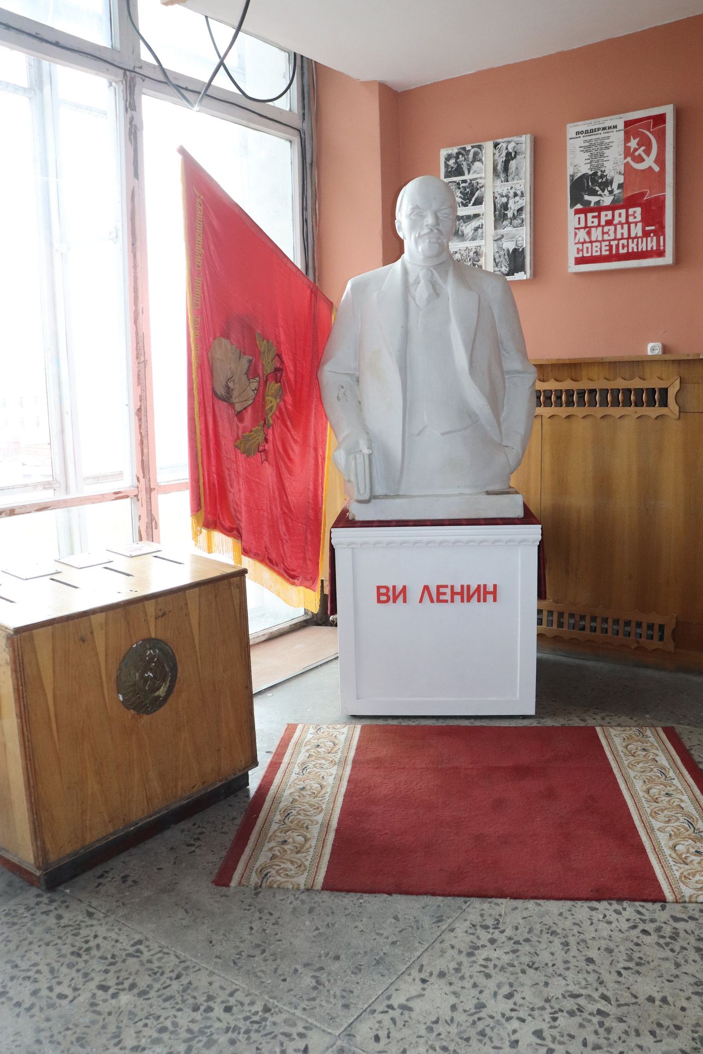 Lenin indoors on a red carpet between two flags