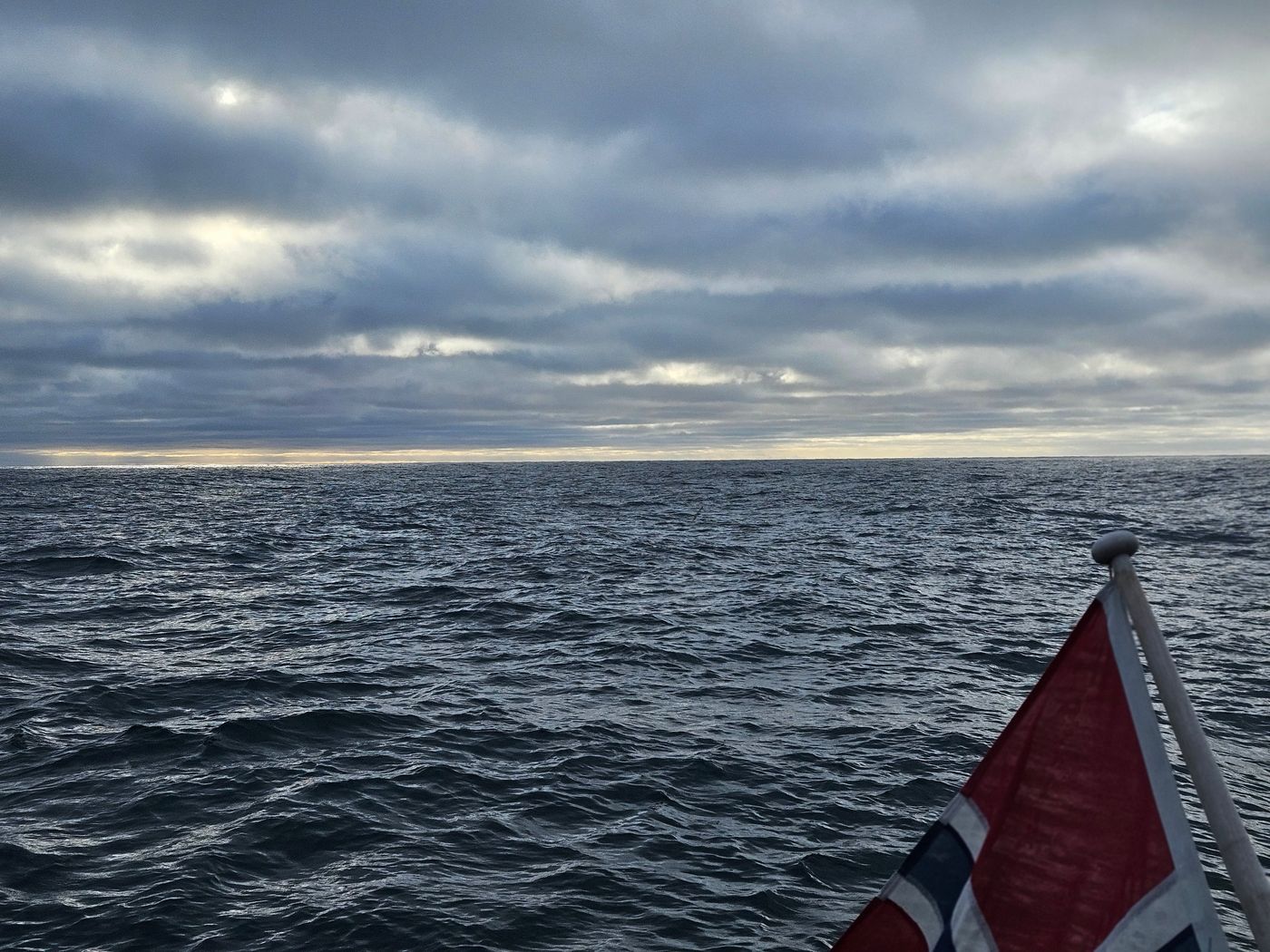 The ensign hard out under a bruised Barents sky